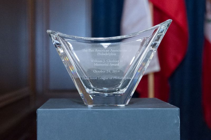 A glass award resting on a dark pedestal. The glass panel is engraved with an inscription that reads: The Pan American Associaton of Philadelphia William J. Clothier II Memorial Award, October 24, 2014, The Union League of Philadelphia.